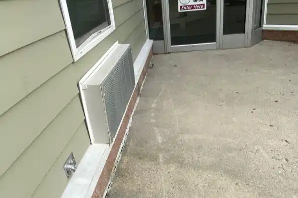 After: Sidewalk leading to a glass door entrance, with an HVAC unit mounted on the wall next to the door.