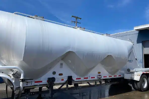 After: A large, silver tanker trailer parked beside a building under a blue sky with a few clouds.