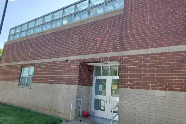 After: Exterior view of a brick building with a glass roof portion and a door featuring a ramp and a small red object nearby.