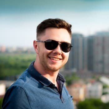 Smiling person wearing sunglasses and a blue shirt, with a cityscape and green landscape in the background.