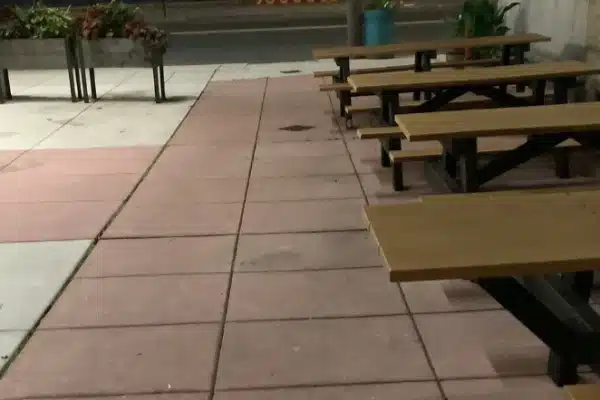 Before: Outdoor seating area at night with wooden tables, concrete pavement, and planters with greenery.