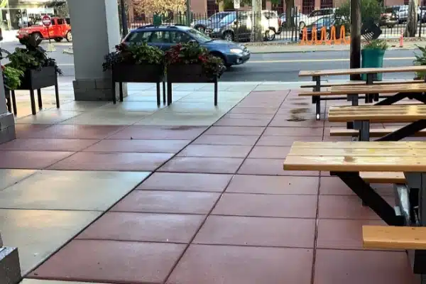 After: Outdoor seating area with picnic tables, potted plants, and a walkway; a car is visible on the street nearby.