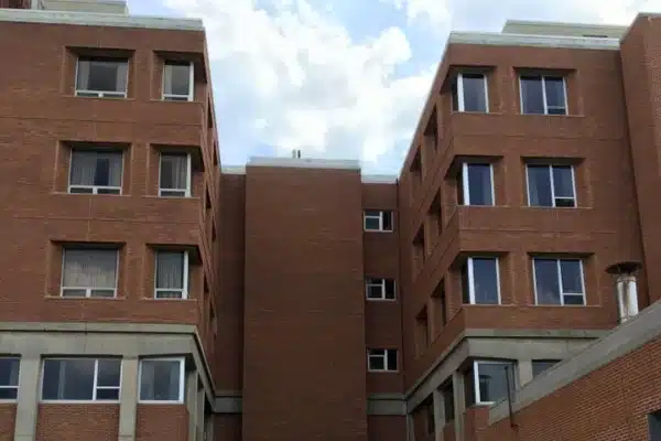 After: Brick building with multiple windows, set against a partly cloudy sky. Structure features a plain façade and concrete base.